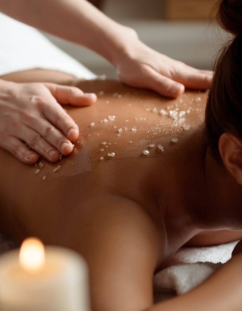 Hands working a sea-salt scrub into a guest’s back